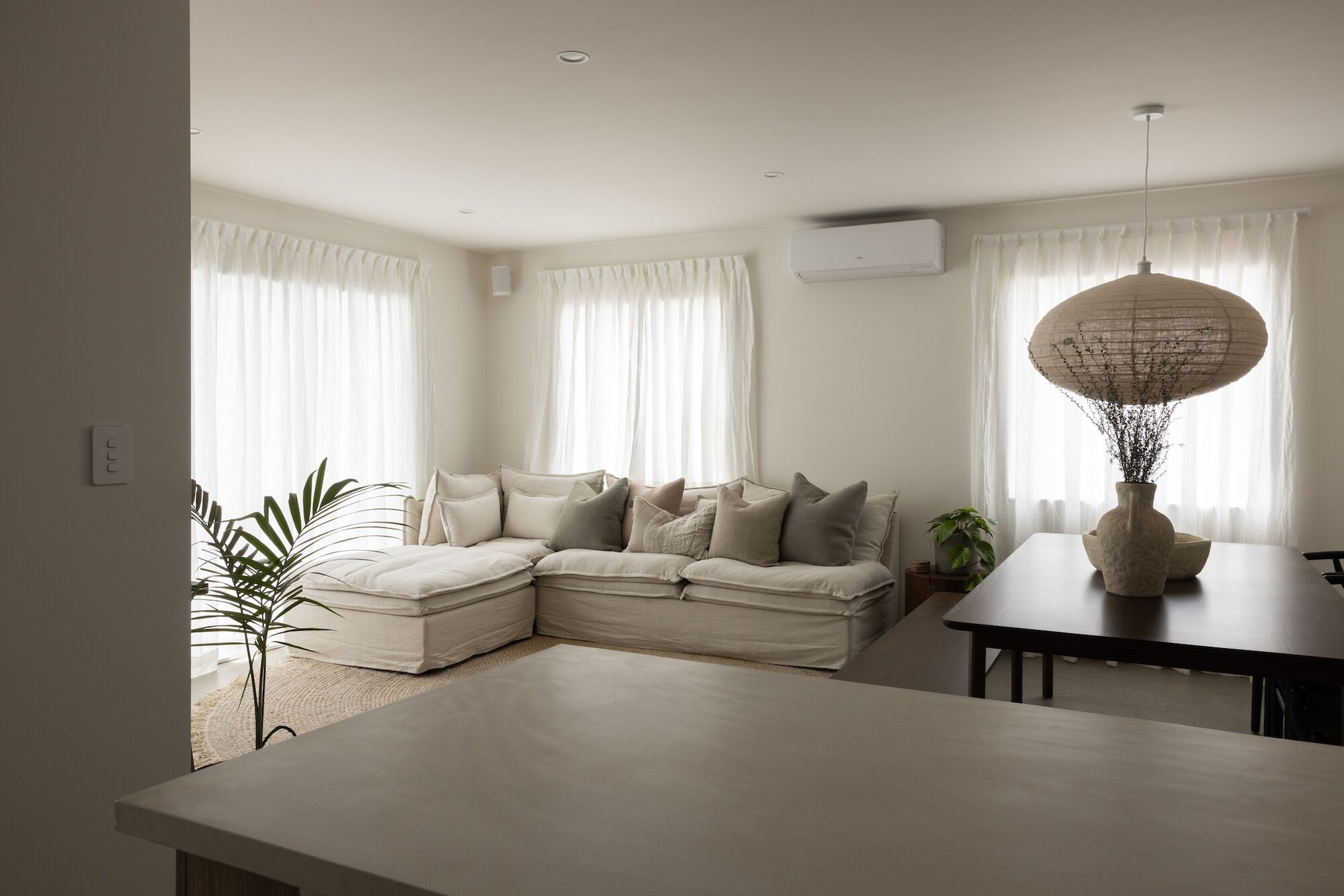 A modern living room with a sectional sofa, a dining table, and a hanging light fixture.