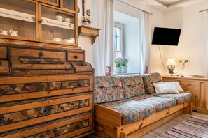 Eine rustikale Holzkommode mit Schubladen, ein gemustertes Sofa, ein an der Wand montierter Fernseher und ein Fenster mit Vorhängen.