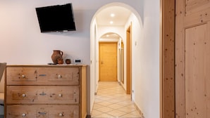 A hallway with a wooden dresser, a television mounted on the wall, and a tiled floor. - Apartment 'Ciasa Majonade Pozza Di Fassa Tipo1' with Mountain View, Private Terrace and Wi-Fi (Pozza di Fassa)