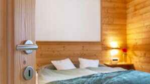 A wooden cabin interior with a bed, a nightstand with a lamp, and a door with a lock. - Apartment 'Ciasa Majonade Pozza Di Fassa Tipo1' with Mountain View, Private Terrace and Wi-Fi (Pozza di Fassa)