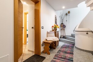 A hallway with a wooden bench, a colorful rug, a small table with flowers, and a staircase.