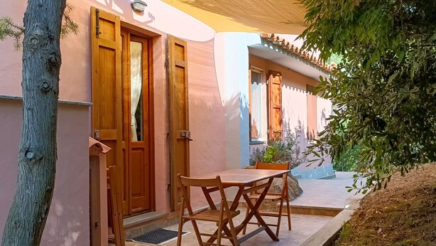 Una mesa y sillas de madera frente a un edificio con paredes rosadas y una puerta.