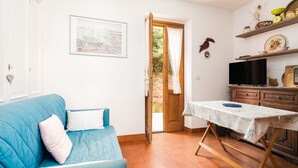 Una habitación con un sofá azul, una puerta de madera, una mesa con mantel y un televisor sobre un mueble de madera.