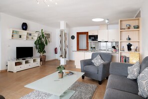 Un salon moderne doté d’un téléviseur à écran plat, d’une table basse, d’un canapé gris et d’un coin cuisine avec un four à micro-ondes.