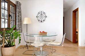 Un coin repas comprenant une table en verre, quatre chaises, une plante en pot, une lampe et un élément décoratif mural.