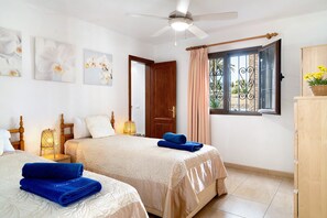Une chambre d’hôtel avec deux lits, un ventilateur de plafond, une fenêtre avec des rideaux et des œuvres d’art accrochées au mur.