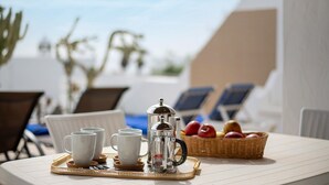 A table with a coffee maker, cups, and a fruit basket, set on a terrace with chairs and a view of the sky. - Vacation Apartment 'Puerto Chico H' with Shared Pool, Private Terrace and Wi-Fi (Playa Blanca)