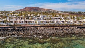 A coastal resort with multiple white buildings, a rocky shoreline, and a mountain in the background. - Vacation Apartment 'Puerto Chico H' with Shared Pool, Private Terrace and Wi-Fi (Playa Blanca)
