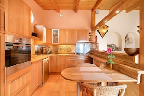A modern kitchen with wooden cabinets, stainless steel appliances, and a dining area with a wooden table and wicker chairs.