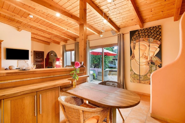 A wooden interior with a dining area, a TV mounted on the wall, and a Buddha painting.
