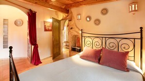 Ein Schlafzimmer mit Bett, Holzbalkendecke, Steinwand und einer Treppe zu einem weiteren Raum.