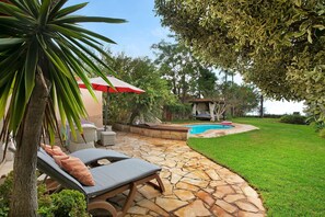 Un patio de piedra con sillones de descanso, una piscina y un césped bien cuidado.