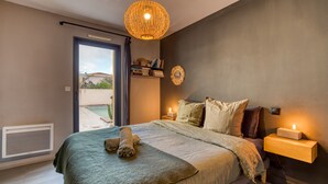 A bedroom with a bed, bedside table, wall-mounted shelf, and a view of the outdoors.