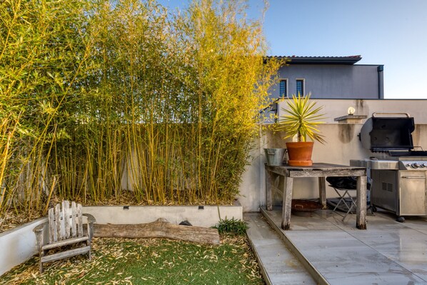 A patio with a grill, a potted plant, and bamboo plants.