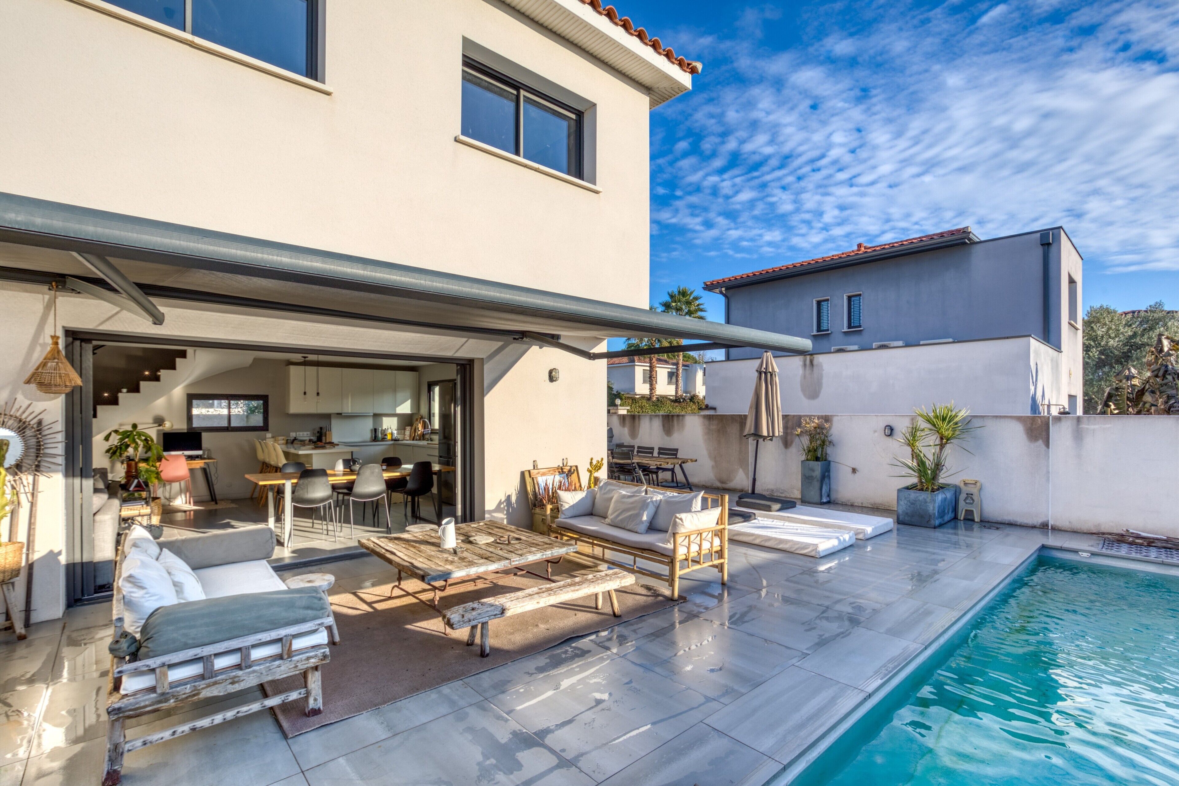 Una casa moderna con piscina, area relax esterna e cucina visibile attraverso un'apertura.