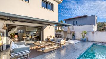Una casa moderna con piscina, area relax esterna e cucina visibile attraverso un'apertura.