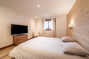 A bedroom with a large bed, a TV on a wooden dresser, a chair, and a window with curtains. - Chalet 'De La Joux' with Private Terrace and Wi-Fi (Saint Sigismond)