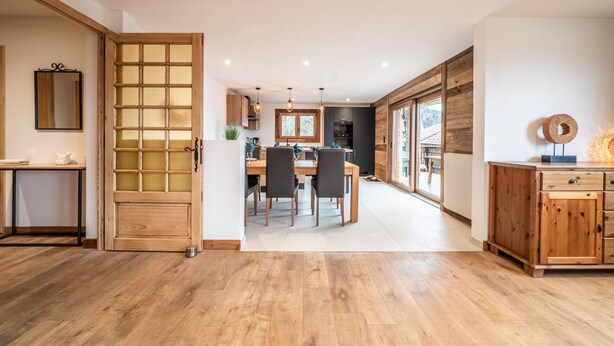 Una cocina amplia con armarios de madera, un comedor con mesa y sillas, y un gran ventanal corredero que da a un balcón.
