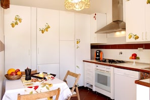 A kitchen with white cabinets, a stove, a dishwasher, and a table with a fruit basket.