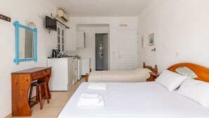 Een slaapkamer met een bed, een houten bureau, een stoel, een televisie en een kitchenette.
