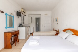 Een slaapkamer met een bed, een houten bureau, een stoel, een televisie en een kitchenette.