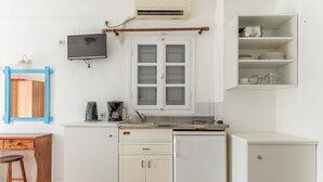 Een kleine keuken met een koffiezetapparaat, een koelkastje en een raam met zonwering.