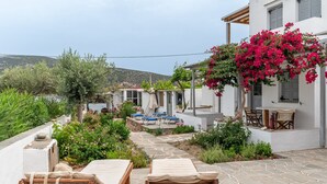 Una villa con patio de piedra, mobiliario exterior y vista al mar.