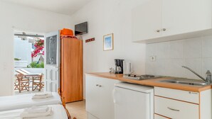 Cocina compacta con lavamanos, cafetera y refrigerador pequeño. Se aprecia un mueble de madera con un televisor encima.