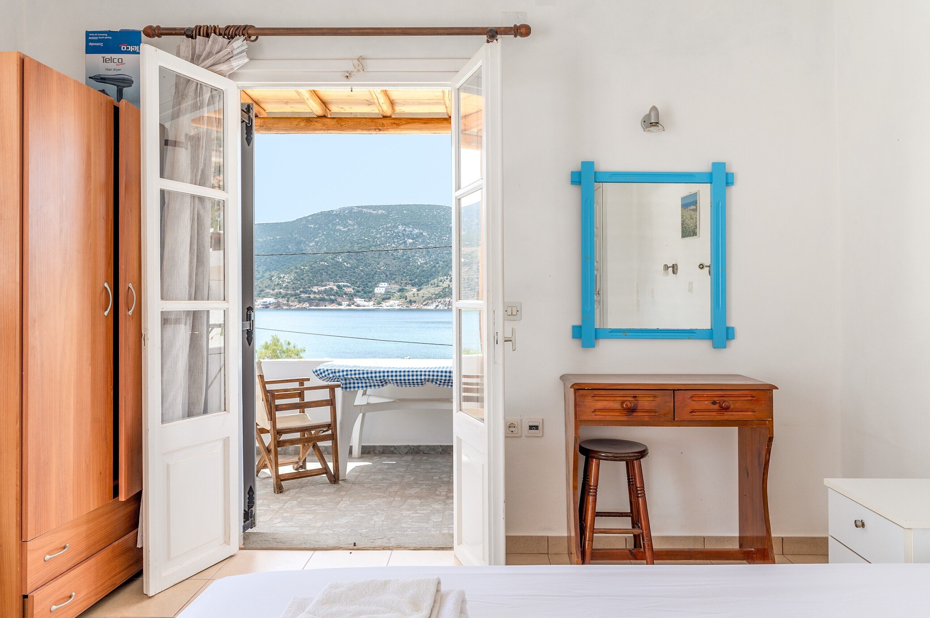 Quarto com cama, escrivaninha, cadeira, guarda-roupa e vista para o mar e as colinas.