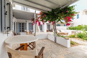 A covered outdoor seating area with a table and chairs, a stone floor, and a view of the building's interior.