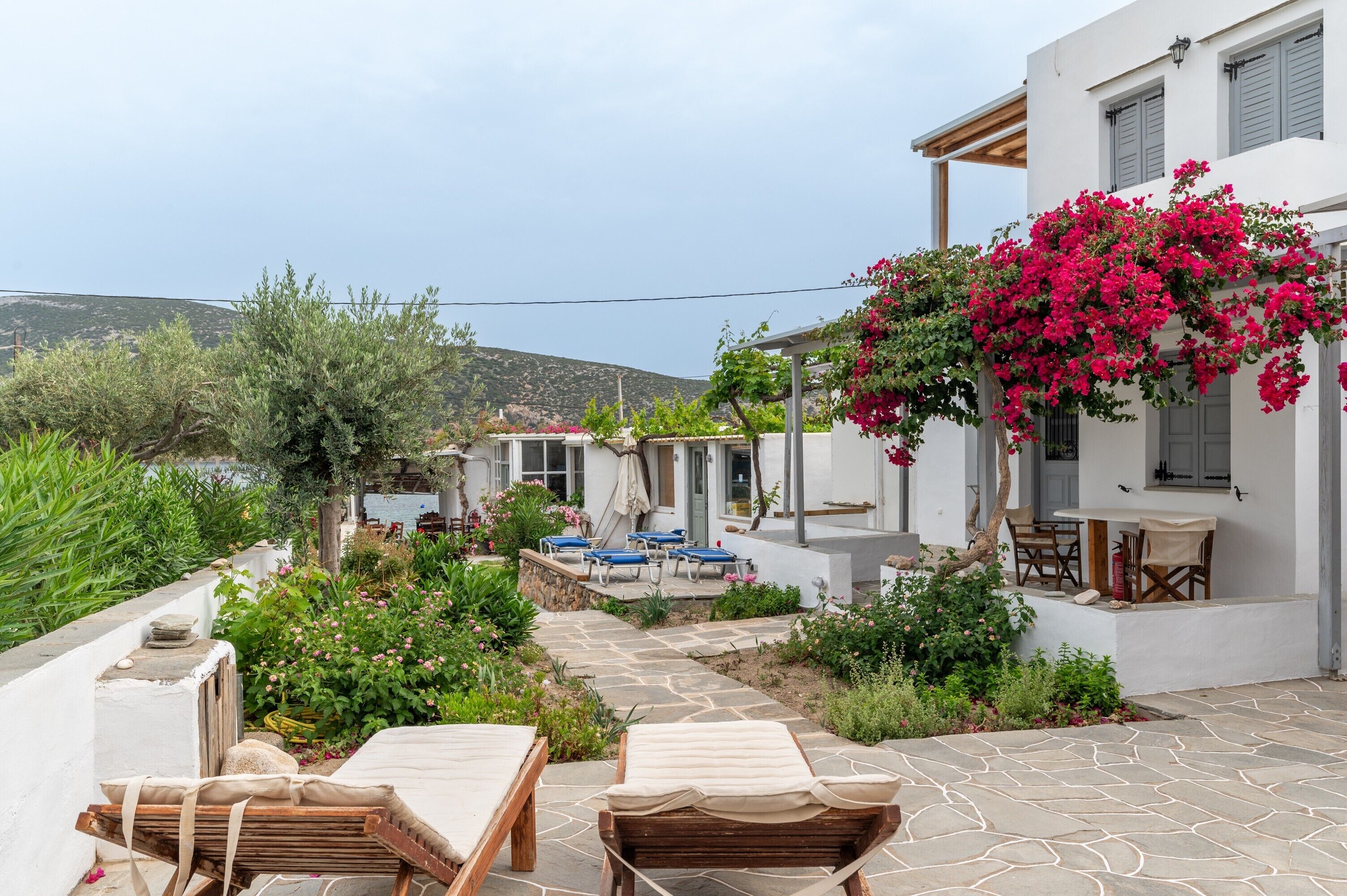 Eine Villa mit einer Steinterrasse, Sitzgelegenheiten im Freien und Blick auf das Meer.