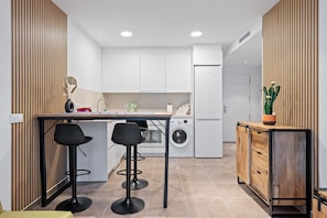 Een moderne keuken met een centraal eiland, barkrukken, een wasmachine en een koelkast.