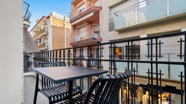 A balcony with a table and chairs, a railing, and a view of a building with balconies and a shop with mannequins. - Apartment 'Mabicarent Playa 2' with Private Terrace, Wi-Fi and Air Conditioning (Calafell)