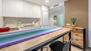 A modern kitchen with white cabinets, a wooden table with a striped placemat, a sink, and a green plant. - Apartment 'Mabicarent Playa 2' with Private Terrace, Wi-Fi and Air Conditioning (Calafell)