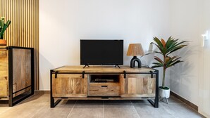 A wooden TV stand with a flat-screen TV, a lamp, and a potted plant. - Apartment 'Mabicarent Playa 2' with Private Terrace, Wi-Fi and Air Conditioning (Calafell)