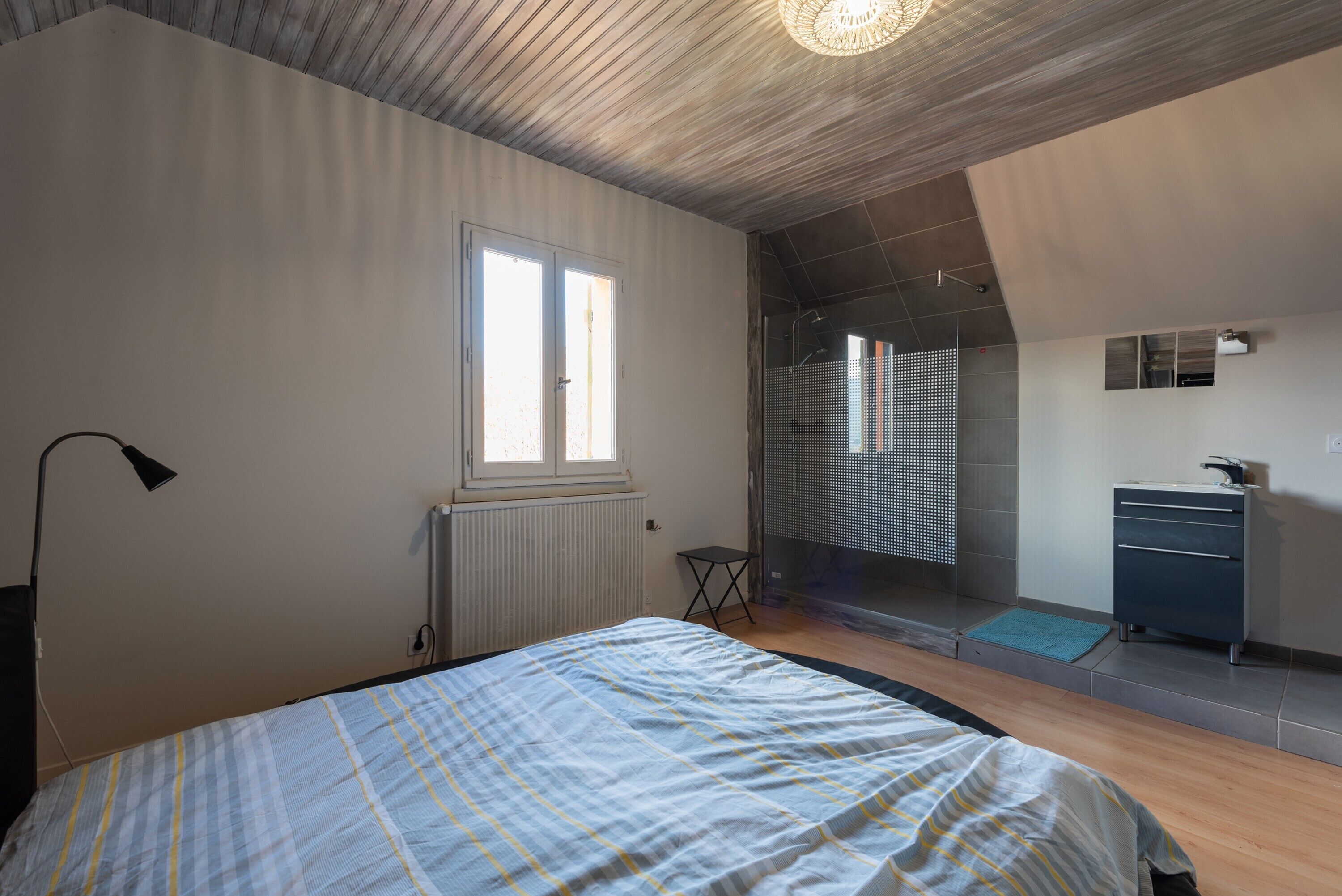 Un dormitorio con cama, ventana, radiador, escritorio y espejo.