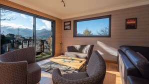 Un salon moderne comprenant un canapé, des fauteuils, une table basse et de grandes fenêtres donnant sur un paysage montagneux.