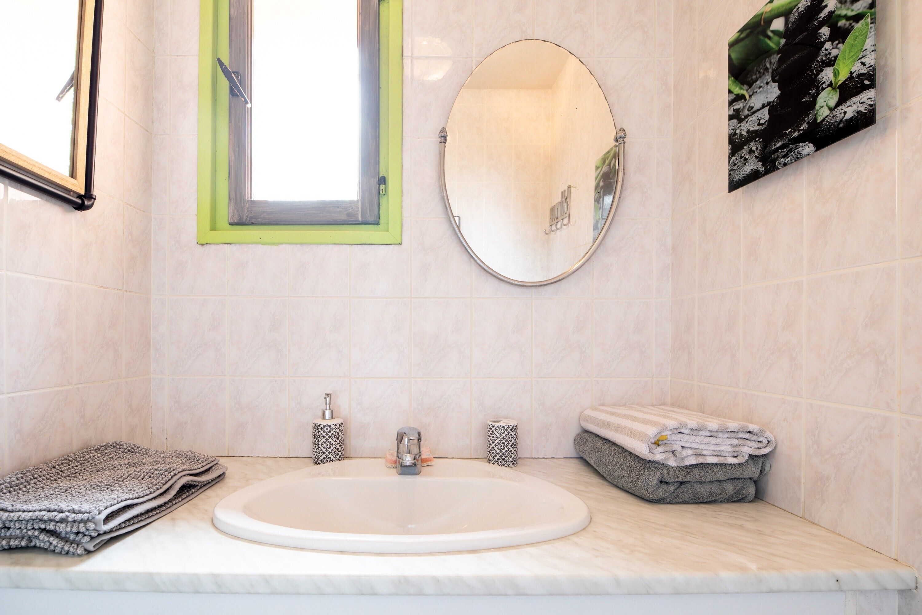 A bathroom with a sink, mirror, window, and towel storage.