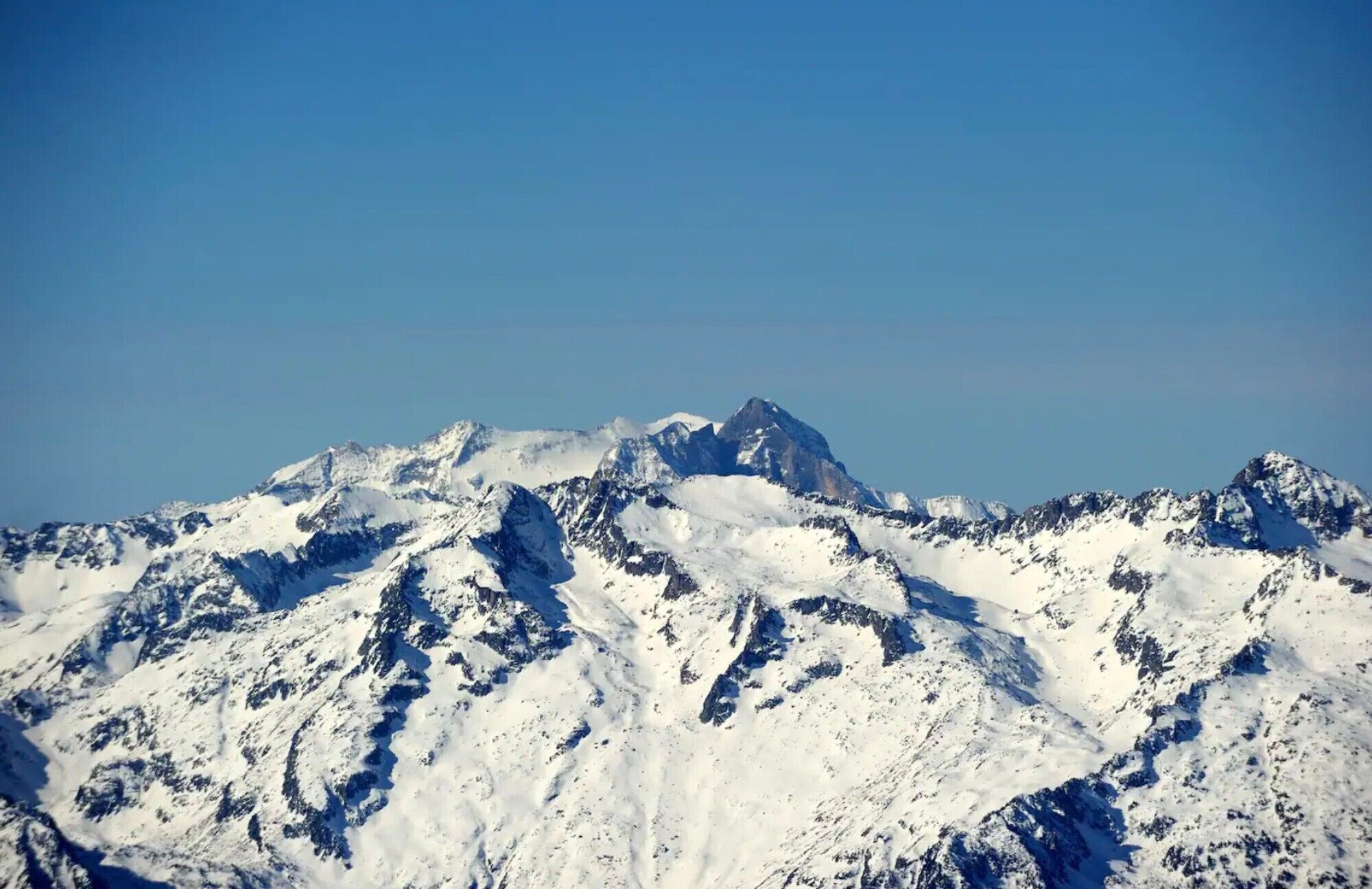 Een met sneeuw bedekte bergketen met ruige toppen en een helderblauwe lucht.
