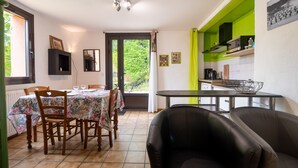 A dining area with a table and chairs, a kitchen with a green accent wall, and a view through a door.