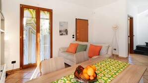A living room with a sofa, a dining table with a fruit bowl, a chandelier, and a sliding glass door. - Apartment 'Ca' Du Barba' with Private Terrace, Private Garden and Wi-Fi (Taggia)