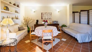 Ein Wohnzimmer mit einer Couch, einem Esstisch mit Stühlen, einer Lampe und Regalen mit Dekoration.