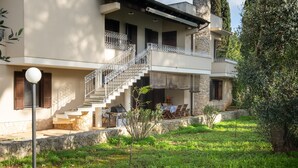Ein zweistöckiges Gebäude mit einer Stein-Fassade, einem Balkon mit Metallgeländern und einer kleinen Außenbereich-Sitzgelegenheit mit Tisch und Stühlen.