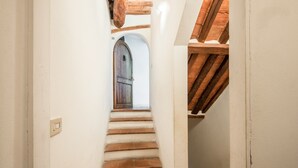 Un escalier étroit mène à une porte en bois, avec un mur blanc d’un côté et un plafond en bois de l’autre.
