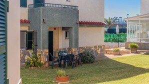 A two-story building with a balcony, a patio with chairs, and a small garden area. - Cala En Forcat Apartment with Shared Pool, Communal Terrace, and Wi-Fi (Menorca)