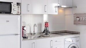 A modern kitchen with a built-in microwave, coffee machine, sink, and washing machine. - Cala En Forcat Apartment with Shared Pool, Communal Terrace, and Wi-Fi (Menorca)