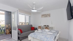 A room with a dining table set for two, a sofa, a ceiling fan, and a TV mounted on the wall. - Cala En Forcat Apartment with Shared Pool, Communal Terrace, and Wi-Fi (Menorca)