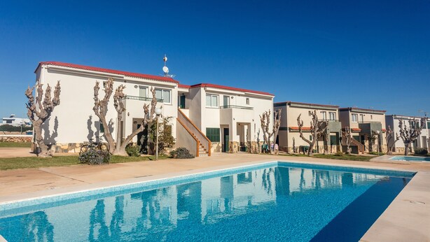 A residential area with a swimming pool, white buildings with red roofs, and cacti. - Cala En Forcat Apartment with Shared Pool, Communal Terrace, and Wi-Fi (Menorca)