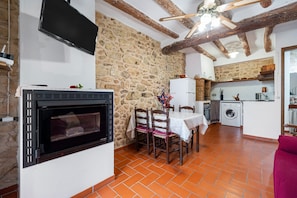 Une cuisine rustique avec un mur en pierre, un four encastré et un coin repas comprenant des chaises et une table.