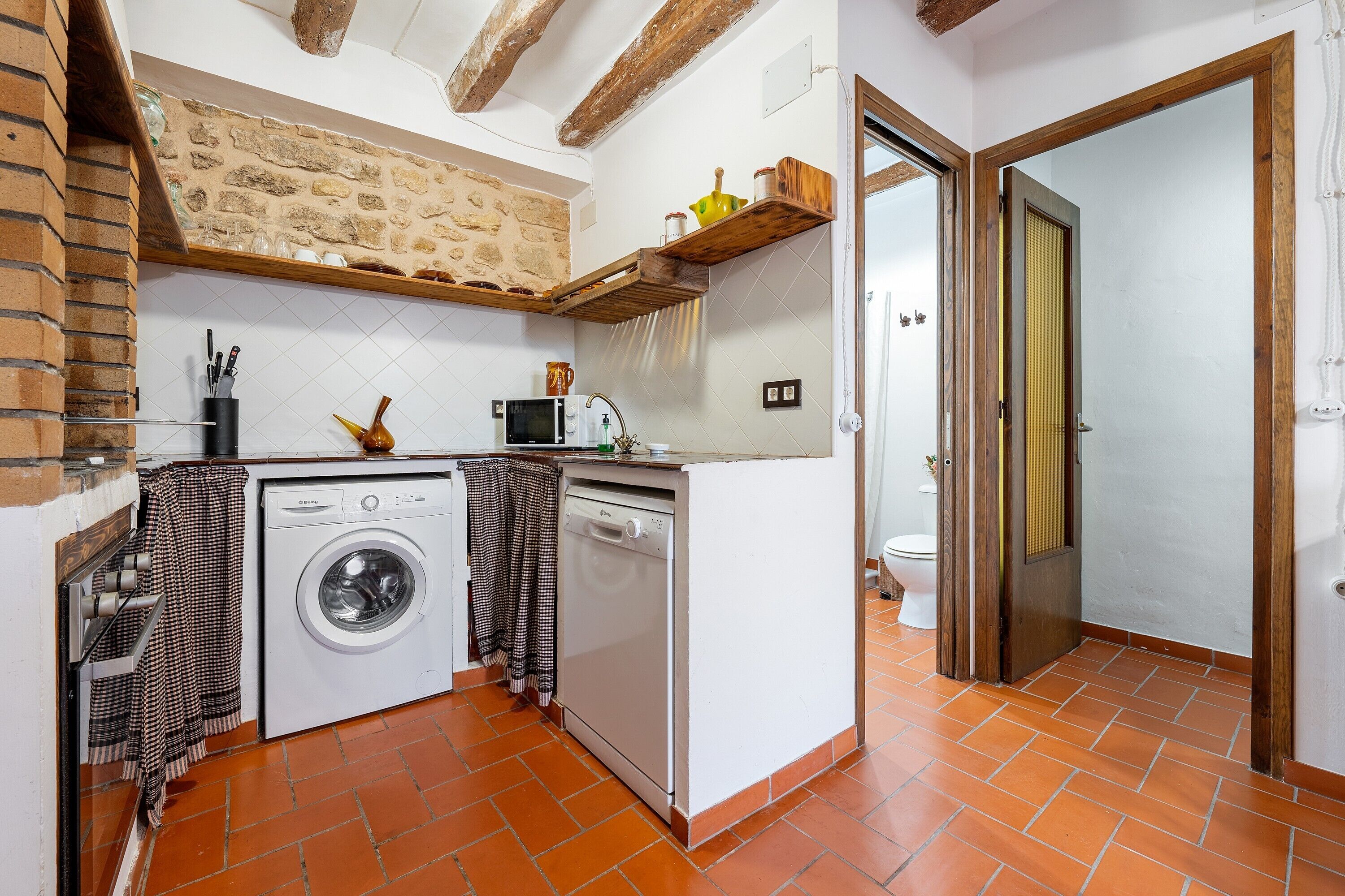 A compact kitchen with a washing machine, microwave, and wooden shelves.